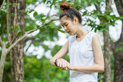 Woman watching time while standing against trees