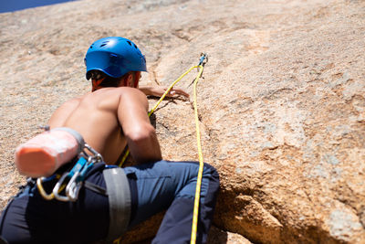 Low angle view of young man climbing rock during sunny day