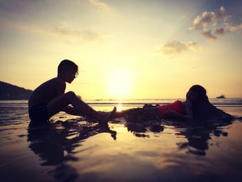Siblings playing on sandy beach during sunset