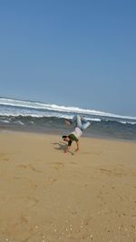 Mid adult man doing handstand at beach against clear blue sky during sunny day