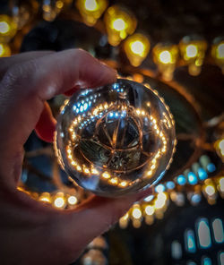 Cropped hand holding crystal ball against illuminated lights at night