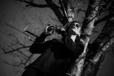 Low angle view of woman standing against bare tree