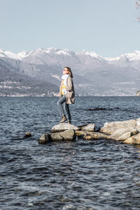 Man standing on rock by sea against mountain