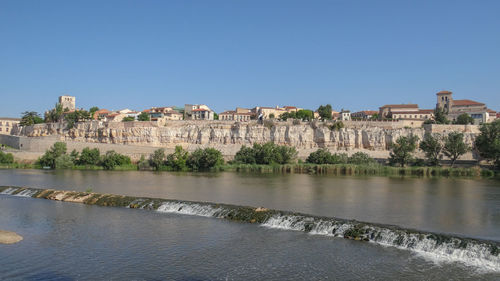 Buildings by river against clear blue sky