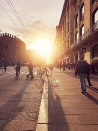 People walking on road amidst buildings in city during sunset