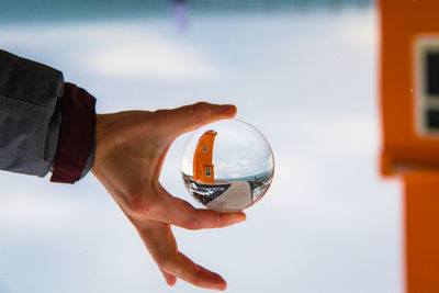 Cropped hand holding crystal ball against sky