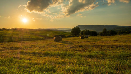 Hay bales on field against sky during sunset