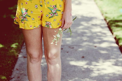 Midsection of woman holding flowers while standing on footpath at park