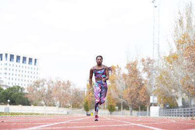 Female athlete running on track against clear sky