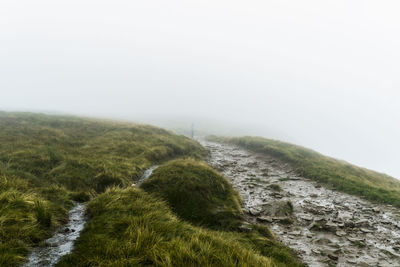 Scenic view of path on grassy hill in foggy weather