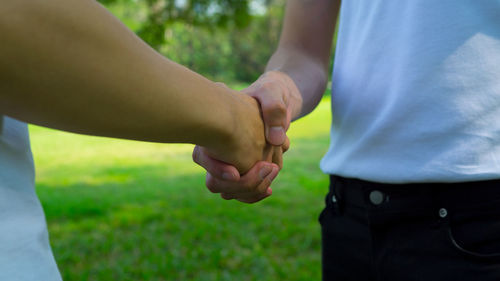 Midsection of friends shaking hands on grassy field