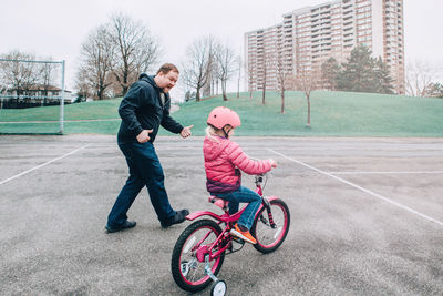 Full length of man encouraging daughter in riding bicycle on walkway