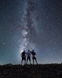 Rear view of friends showing buttocks while standing on stone wall against star field