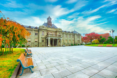 Park bench by building against sky during autumn