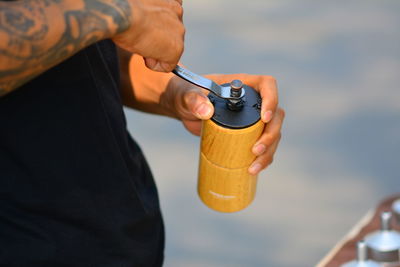 Midsection of man holding bottle against water