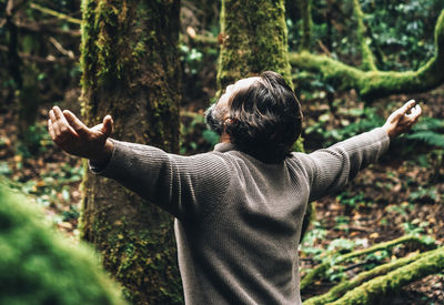 Rear view of man with arms outstretched standing against trees