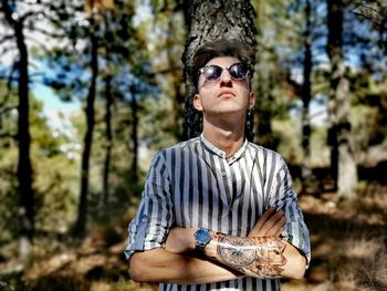 Young man wearing sunglasses standing against tree in forest