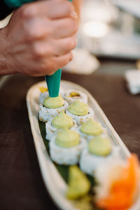 Vertical view of the hands of unknown chief decorating tasty rolls with japanese wasabi sauce