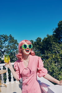 Portrait of young woman wearing sunglasses against clear blue sky