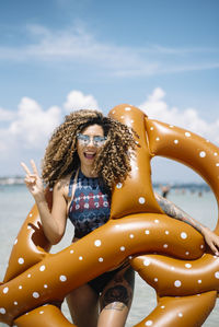 Portrait of smiling woman holding pool raft while standing at beach