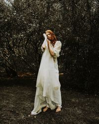 Young woman wearing dress standing against tree in forest