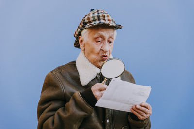 Close-up of senior woman examining paper with magnifying glass against blue background