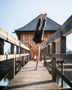 Man doing handstand on footbridge against clear sky