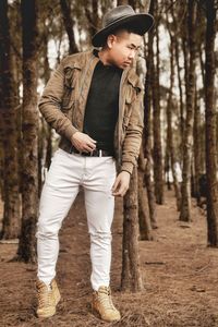 Full length of man standing by tree trunk in forest