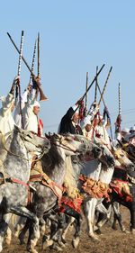 People raiding guns while riding horses against clear sky