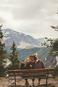 Rear view of friends sitting on bench against mountain