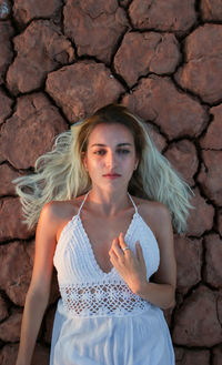 Beautiful young woman with blonde hair and dressed in white lying on the cracked ground 