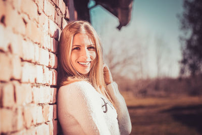 Portrait of smiling young woman leaning against brick wall