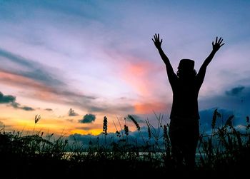 Silhouette woman with arms raised against sky during sunset