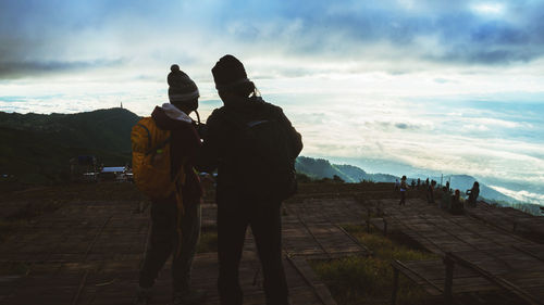 Rear view of people standing on mountain against sky