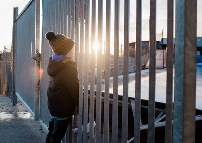 Young boy looking out at an ice rink at sunset with his skates