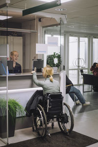 Female patient sitting on wheelchair and doing inquiry with receptionist at healthcare center