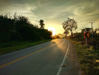 Road by trees against sky during sunset