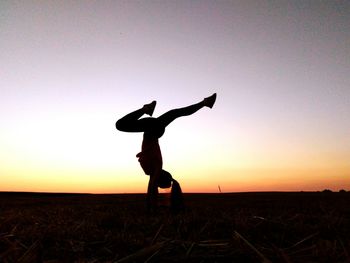 Silhouette woman doing handstand against clear sky during sunset