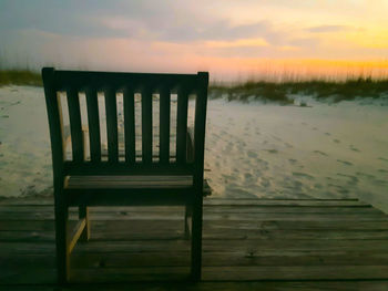 Chair on beach against sky during sunset