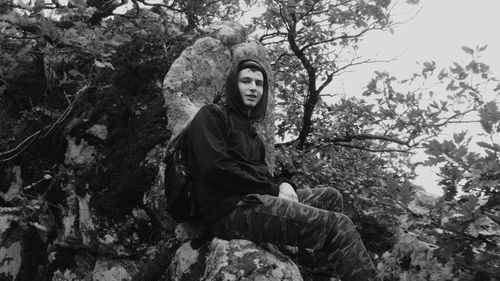 Portrait of young woman looking away while sitting on rock