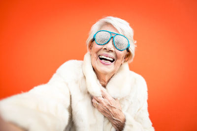 Portrait of cheerful senior woman wearing sunglasses against orange background