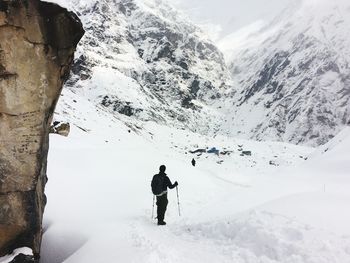 Rear view of man holding ski poles standing on snow covered field