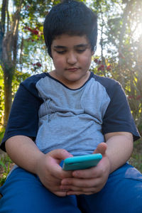 Boy holding mobile phone sitting outdoors
