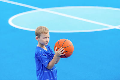 Boy holding basketball while standing on sports court