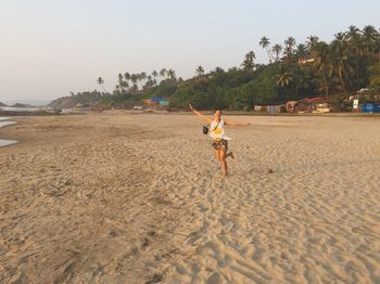 Full length of playful woman standing at sandy beach during sunset