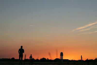 Silhouette people standing on street against sky during sunset