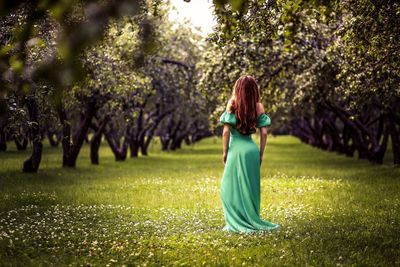 Rear view of young woman standing on grassy field amidst trees