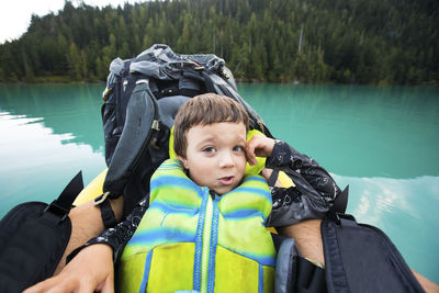 Boy wearing pfd rests against backpack on inflatable boat on blue lake