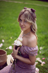 Portrait of a beautiful young woman sitting on a green meadow in summer and holding a bouquet 