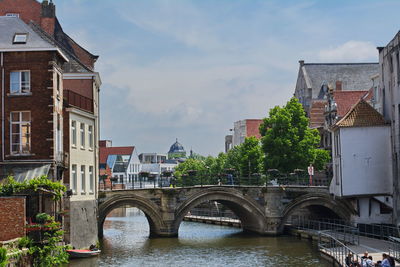 Bridge over river amidst buildings in city against sky